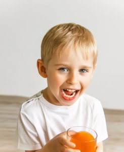 Junge lächelt mit seinem Saft in der Hand. Kleinkinder sind oft betroffen von Pilz im Mund.