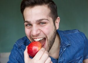 Mann beißt mit gesunden Zähnen in Apfel