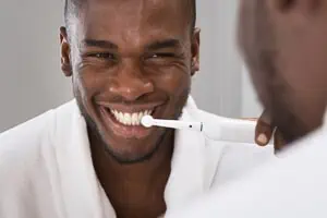 Mann putzt weiße Zähne mit elektrischer Zahnbürste