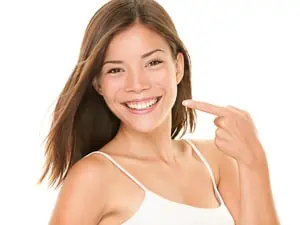 Frau zeigt lächelnd auf ihre weißen Zähne