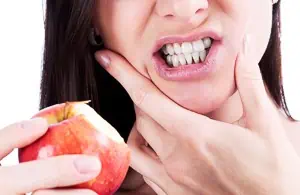 Frau mit Zahnschmerzen beißt in Apfel