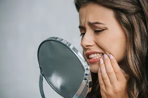 Frau mit Zahnschmerzen blickt in den Spiegel