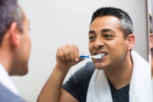 man brushing teeth in mirror