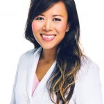 A smiling woman wearing a white coat over a pink shirt, with long hair, against a plain white background.