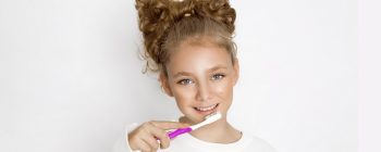 Smiling girl with curly hair holding a toothbrush, promoting dental hygiene against a white background.