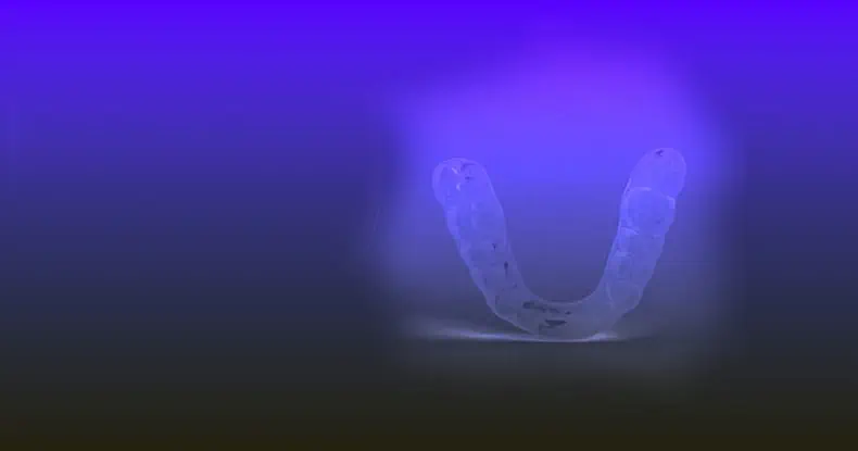 Clear dental aligner on a gradient background, illuminated to highlight its shape and design.