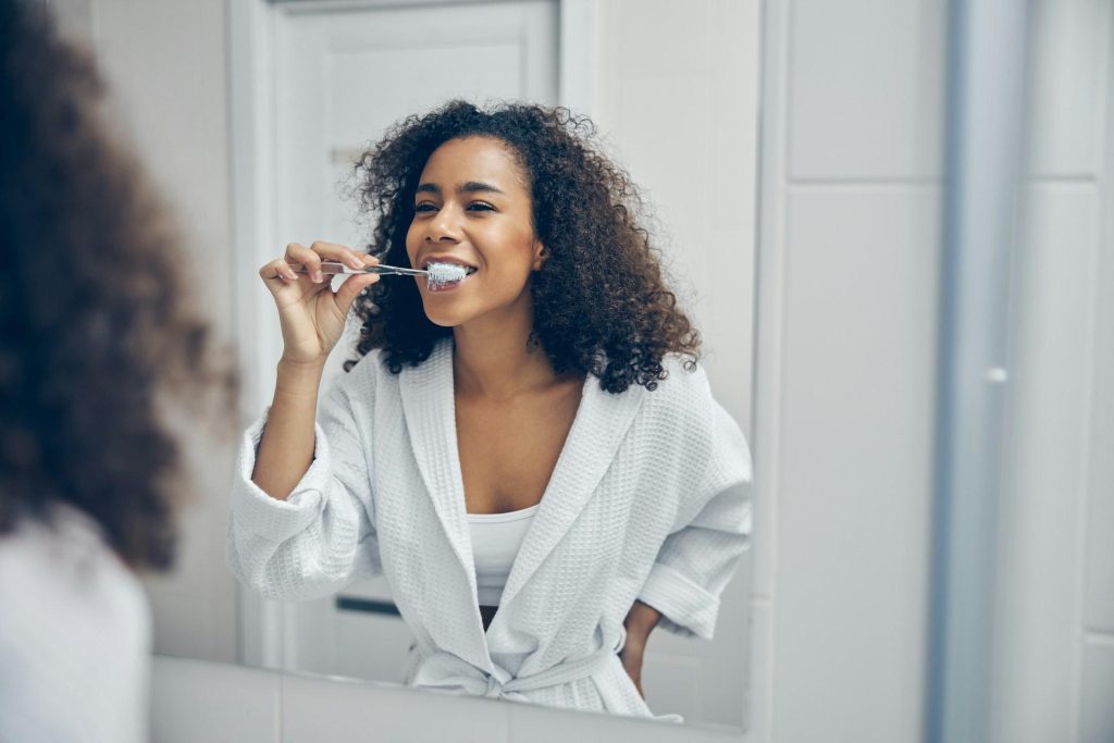 Woman brushing her teeth in front of a bathroom mirror