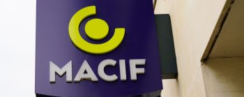 Sign for MACIF featuring a yellow circular logo on a purple background, displayed on a building's exterior.